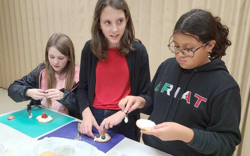 MAKING MUNCHIES—Ochiltree County 4-H members participating in the Fun with Food program got together this week to learn how to bake chocolate chip cookies and fruit pizzas. Pictured assembling their fruit pizzas are, from left, Kendall DeWitt, Brooke Helker, and Allizay Barraza