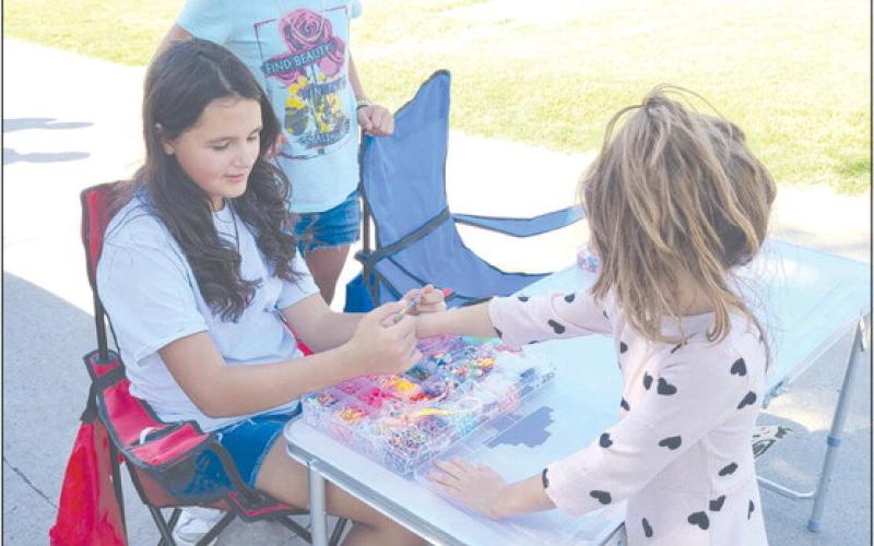 Young entrepreneurs can take many different roads to find success. In the case of Gianna Reyes, age 10, at left, and Brisaedi Garcia, 10, their version of the curbside lemonade stand is more of a bracelet stand — they’ve been creating bracelets for kids, including five-year-old Marissa, who’s getting her new bracelet fitted for size, who come by their table at 1010 S. Drake.
