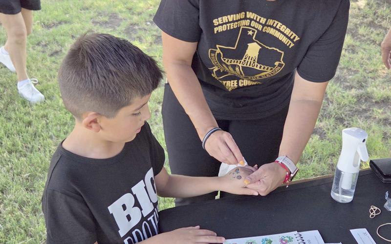 Perryton residents turned out last Thursday evening to enjoy the Perryton Ochiltree Chamber of Commerce’s annual block party on Main Street and on the courthouse lawn. Among the groups offering fun and activities to locals was the Ochiltree County Sheriff’s Department, which had fingerprinting kits, stickers, and temporary tattoos. Pictured are Daymian Godoy, age 6, receiving a temporary tattoo from volunteer Kim Rios.