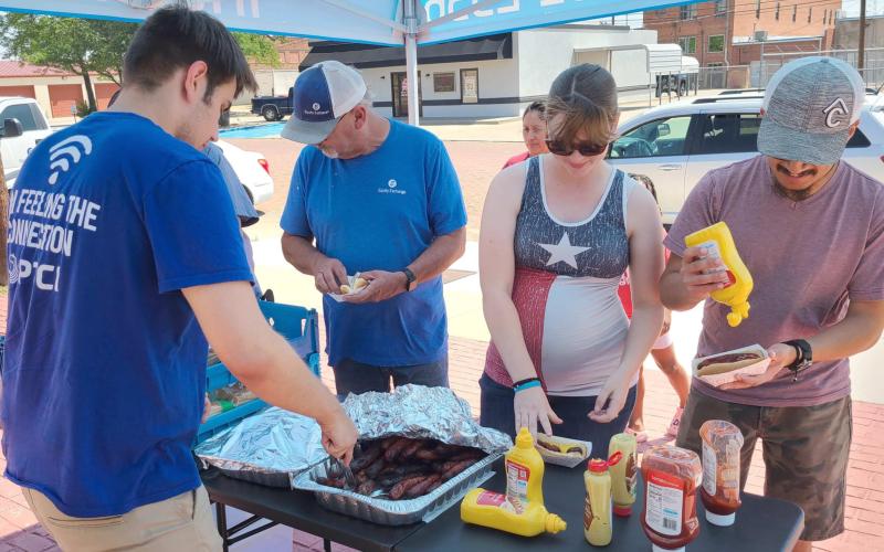LUNCH ON A HOT DAY—Staff at PTCI held a bratwurst and broadband appreciation lunch last Thursday for customers. Pictured are, from left, Coleman Mathis serving up bratwurst for Charles Crawford, Cindy Escobar, and Miguel Escobar.