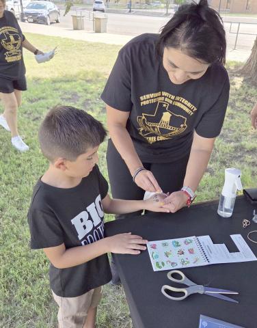 Perryton residents turned out last Thursday evening to enjoy the Perryton Ochiltree Chamber of Commerce’s annual block party on Main Street and on the courthouse lawn. Among the groups offering fun and activities to locals was the Ochiltree County Sheriff’s Department, which had fingerprinting kits, stickers, and temporary tattoos. Pictured are Daymian Godoy, age 6, receiving a temporary tattoo from volunteer Kim Rios.