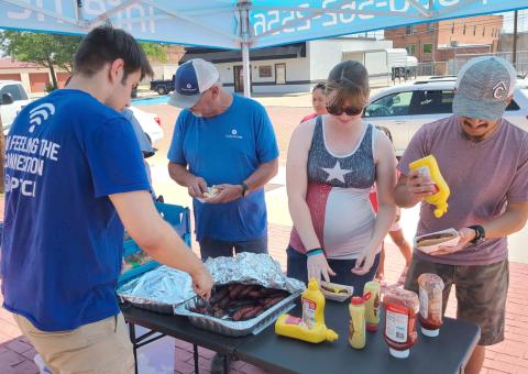 LUNCH ON A HOT DAY—Staff at PTCI held a bratwurst and broadband appreciation lunch last Thursday for customers. Pictured are, from left, Coleman Mathis serving up bratwurst for Charles Crawford, Cindy Escobar, and Miguel Escobar.
