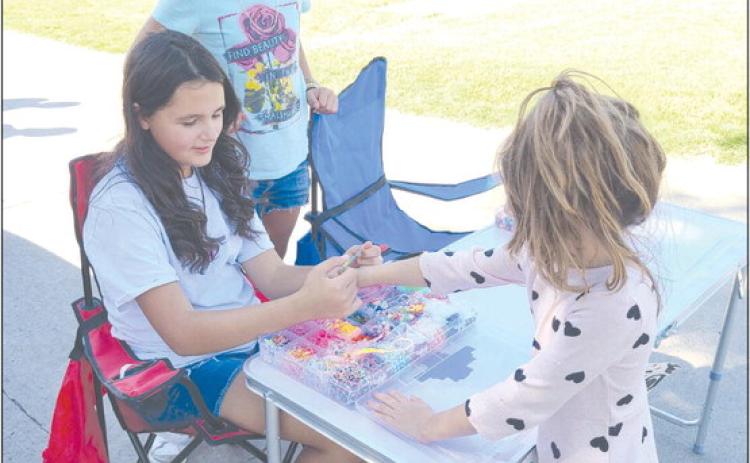 Young entrepreneurs can take many different roads to find success. In the case of Gianna Reyes, age 10, at left, and Brisaedi Garcia, 10, their version of the curbside lemonade stand is more of a bracelet stand — they’ve been creating bracelets for kids, including five-year-old Marissa, who’s getting her new bracelet fitted for size, who come by their table at 1010 S. Drake.