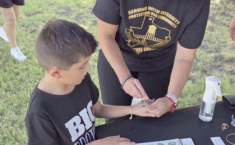 Perryton residents turned out last Thursday evening to enjoy the Perryton Ochiltree Chamber of Commerce’s annual block party on Main Street and on the courthouse lawn. Among the groups offering fun and activities to locals was the Ochiltree County Sheriff’s Department, which had fingerprinting kits, stickers, and temporary tattoos. Pictured are Daymian Godoy, age 6, receiving a temporary tattoo from volunteer Kim Rios.