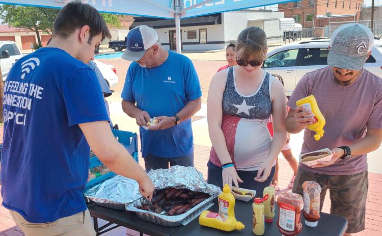 LUNCH ON A HOT DAY—Staff at PTCI held a bratwurst and broadband appreciation lunch last Thursday for customers. Pictured are, from left, Coleman Mathis serving up bratwurst for Charles Crawford, Cindy Escobar, and Miguel Escobar.